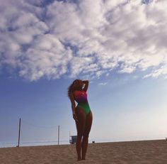 a woman standing on top of a sandy beach under a blue sky with white clouds