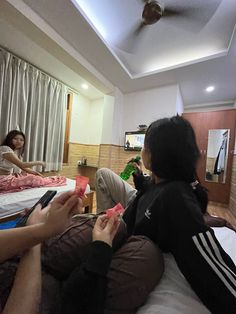 three people sitting on a bed in a room with two other people looking at their cell phones