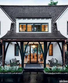 a large white house with black trim and windows on the front door is lit up at night