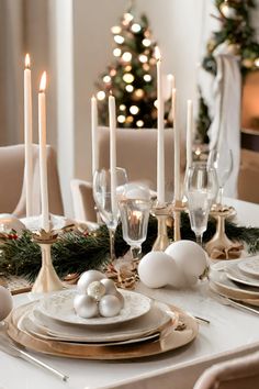 a dining room table set for christmas with white and gold plates, silverware and candles