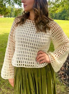 a woman wearing a white sweater and green pleated skirt standing in front of a tree