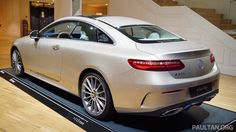 the rear end of a white car on display in a showroom with wooden floors