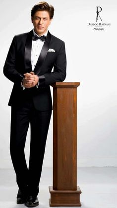 a man in a tuxedo standing next to a podium with his hands folded