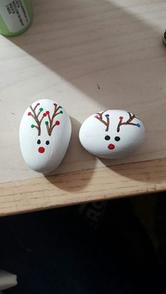 two painted rocks sitting on top of a wooden table next to each other with reindeer noses