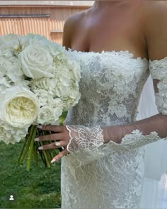 a woman in a wedding dress holding a bouquet of white roses and greenery with her arm wrapped around the bride's shoulder