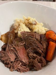 a white bowl filled with meat, potatoes and carrots on top of a table