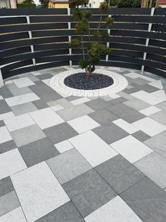 a small tree is placed in the middle of a circular stone area with black and white tiles