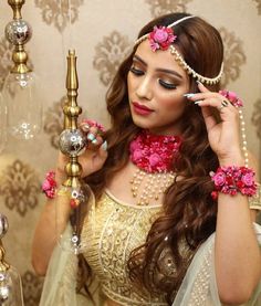 a woman in a white and gold outfit with pink flowers on her head holding a lamp