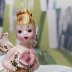 a little figurine sitting on top of a white plate holding a pink rose