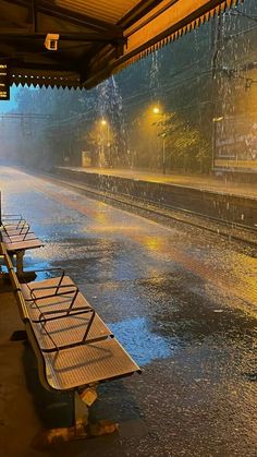 the rain is pouring down on benches at the train station in the evening, and there are no people sitting under them