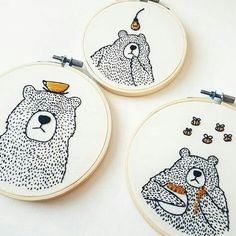 three hand embroidered hoop art with bears and bees on them, one is holding a beehive