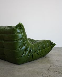 a green bean bag sitting on top of a cement floor next to a white wall