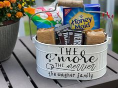 a white bucket filled with chocolates and candy on top of a wooden table next to a potted plant