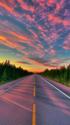 an empty road with trees in the background and colorful clouds above it at sunset or sunrise