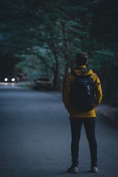 a man with a backpack standing on the side of a road in the middle of the night