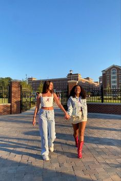 two young women walking down a brick walkway holding hands and wearing white outfits with red boots