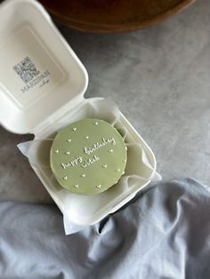 a green cake in a white box on a bed with the lid open and writing happy birthday mom