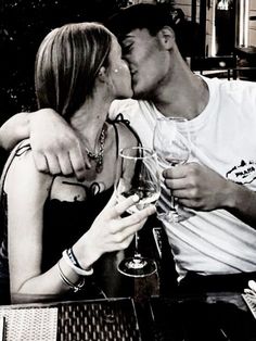 a man and woman kissing while holding wine glasses in front of each other at a table