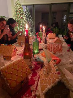 people sitting around a table with gingerbread houses on it and candles in the middle