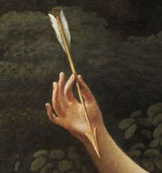 a hand holding a feather with rocks in the background