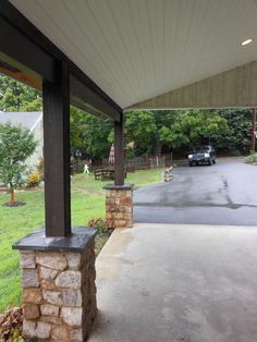 a car is parked in the driveway under a covered porch with stone pillars and columns