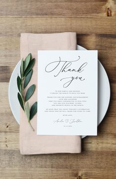 a white plate topped with a napkin next to a green leafy place card on top of a wooden table