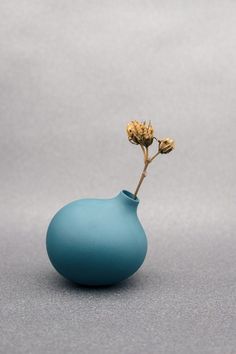 a small blue vase with a single flower in it's center on a gray surface