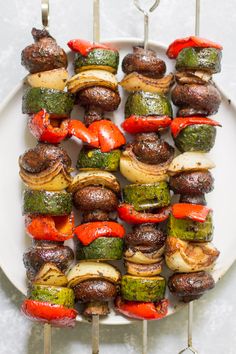 the skewers are covered with vegetables and meats on a white platter