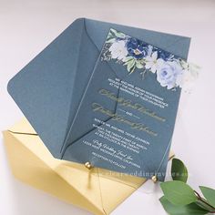 a blue and gold wedding card on top of an origami envelope with flowers