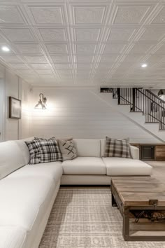 a living room with white couches and wooden coffee table in front of the stairs