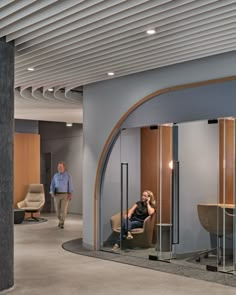 a woman sitting on a chair in a room with glass partitions and two men walking by