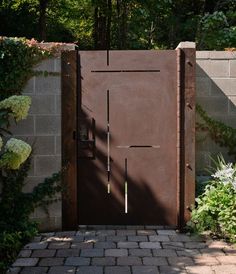 a large brown door in the middle of a brick walkway surrounded by greenery and trees