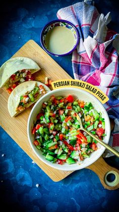 a bowl filled with salad next to pita bread on a cutting board and spoon