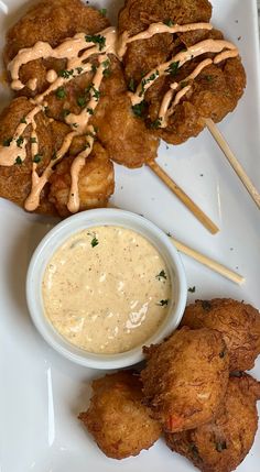 some fried food is on a white plate with dipping sauce and toothpick sticks