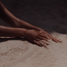 a person laying on the ground with their hands in the sand and one hand reaching for something