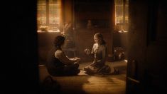 two women sitting on the floor in front of a fire place and one is holding a cup