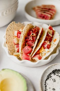 there are three tacos on the table with other plates and bowls around them,