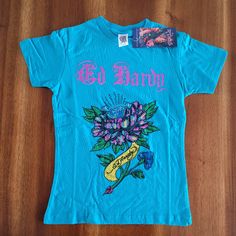 Ed Hardy By Christian Audigier Kids Graphic Tee. Girls Cut Tee. Teal Color With Iconic Design & Rhinestones! 100% Cotton. S = 2/4 Style 5gg204tflg Trendy Blue T-shirt With Embroidered Graphics, Blue Embroidered T-shirt For Summer, Blue Embroidered Tops For Summer, Blue Unisex Shirt With Letter Print, Unisex Blue Graphic Print Top, Unisex Blue Top With Graphic Print, Blue T-shirt With Embroidered Graphics, Unisex Blue Tops With Graphic Print, Blue Graphic Tee With Embroidered Graphics