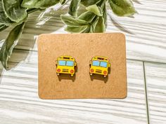 two yellow school bus earrings sitting on top of a piece of paper next to a plant