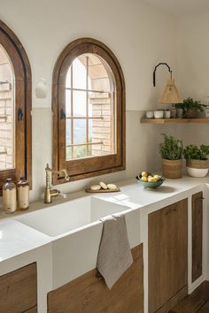 two arched windows in a kitchen with wooden cabinets and white counter tops, along with bowls of fruit on the counter