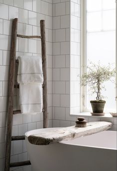 a white bath tub sitting under a window next to a wooden ladder in a bathroom