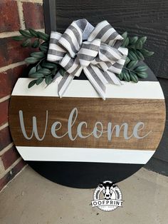 a welcome sign hanging on the side of a brick wall next to a black and white door