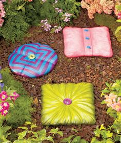 four pillows in the ground surrounded by plants and flowers, all made out of different colors