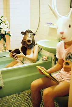 two people sitting in a bathtub with bunny masks on their heads and one person holding a book