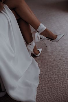 a woman is sitting on the floor wearing high heels and a white dress with straps