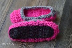 a pair of pink and gray crocheted baby shoes sitting on top of a wooden floor