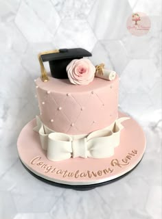 a pink graduation cake with a mortar and rose on top, sitting on a marble table