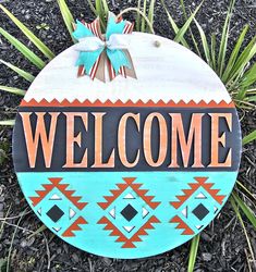 a wooden sign that says welcome in front of some grass and flowers with a bow on it