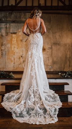 the back of a woman in a wedding dress standing on a wooden bench with her hands behind her back