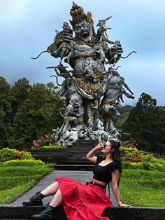 a woman in a red skirt sitting on a bench next to a statue with an elephant